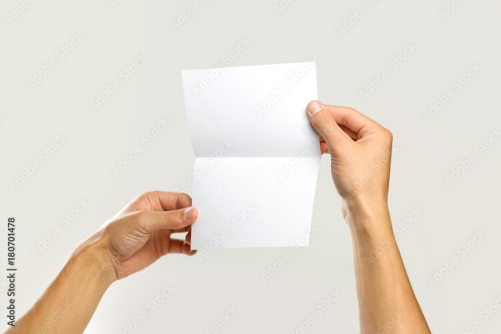 Male hands holding a white sheet of paper. Isolated on gray background. Closeup Male hands holding a white sheet of paper. Isolated on gray background. Closeup