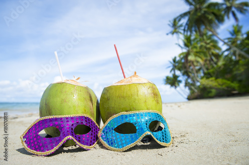 Colorful sequined carnival masks and fresh green coconut drinks on a palm fringed beach in Brazil.