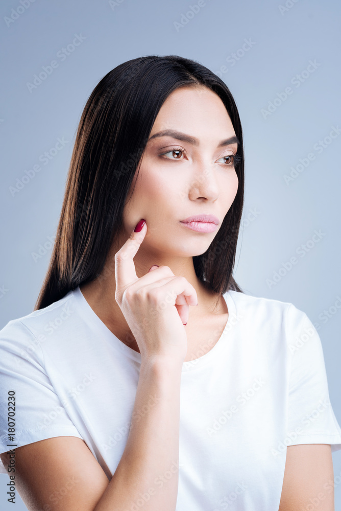 Touch. Serious young beautiful woman feeling offended while standing against the blue background and touching her chick with a finger Touch. Serious young beautiful woman feeling offended while standing against the blue background and touching her chick with a finger