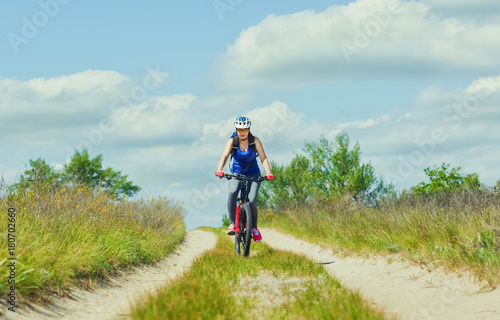Fototapeta Naklejka Na Ścianę i Meble -  One young woman - an athlete in a helmet riding a mountain bike outside the city, on the road on a summer day.