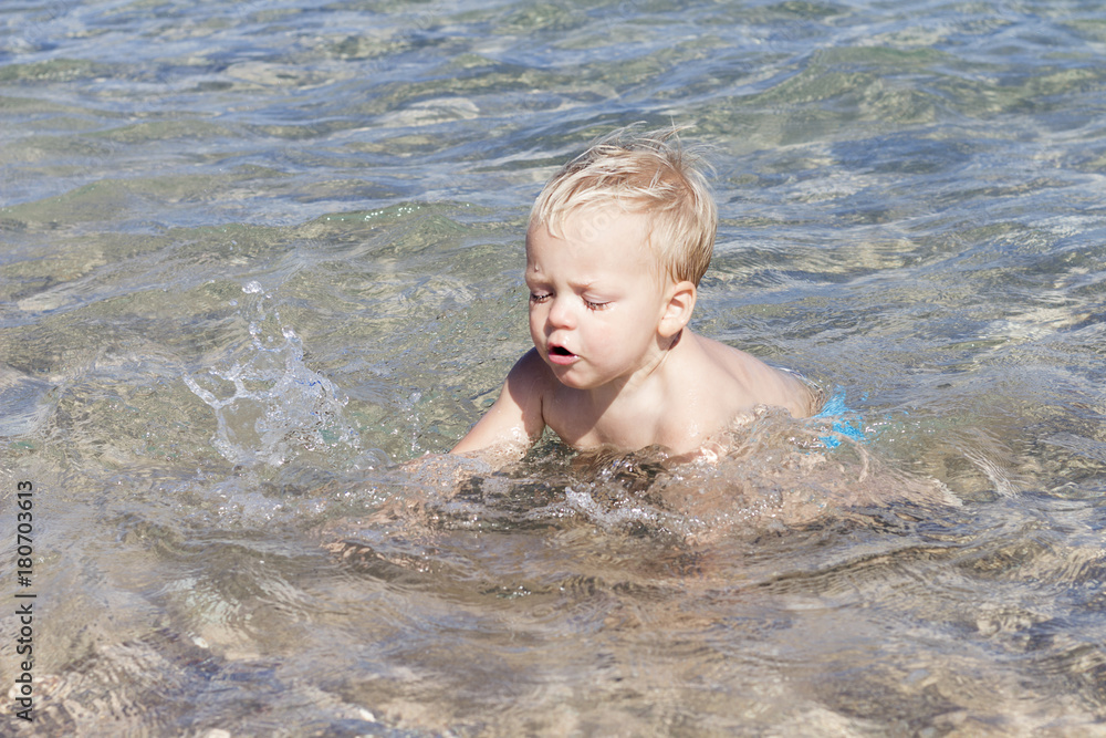 Cute toddler splashing in the water. Funny little kid having fun and trying to swim Cute toddler splashing in the water. Funny little kid having fun and trying to swim