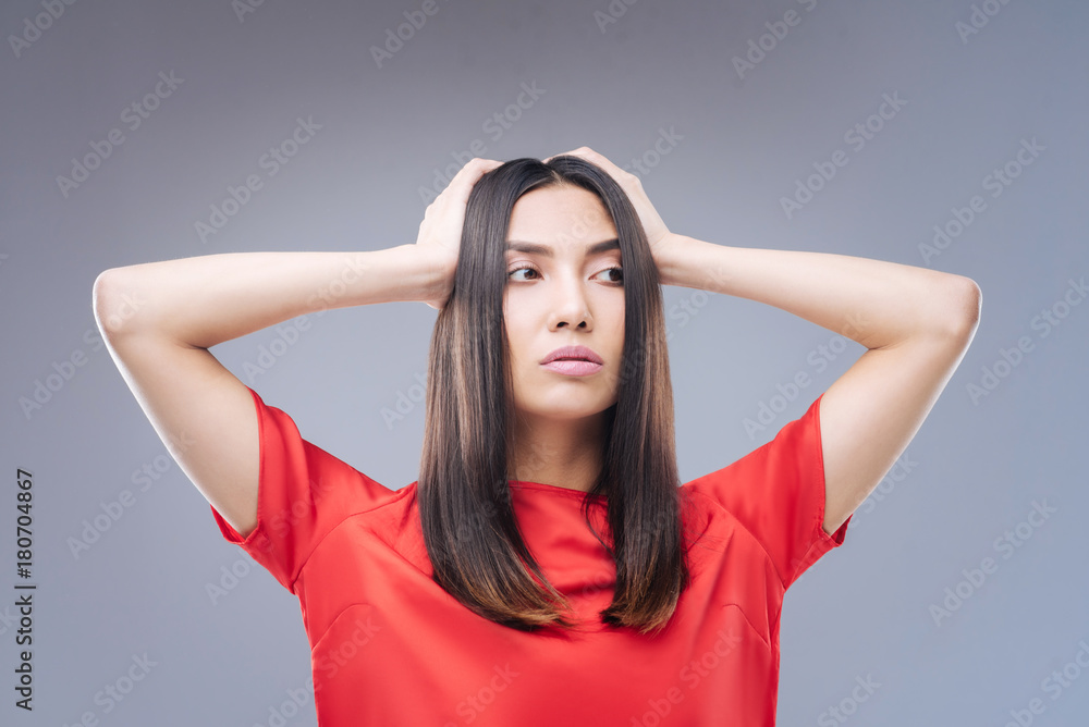 Poor student. Worried beautiful thoughtful student standing alone and touching her head with two hands while having no idea what to do with her life Poor student. Worried beautiful thoughtful student standing alone and touching her head with two hands while having no idea what to do with her life