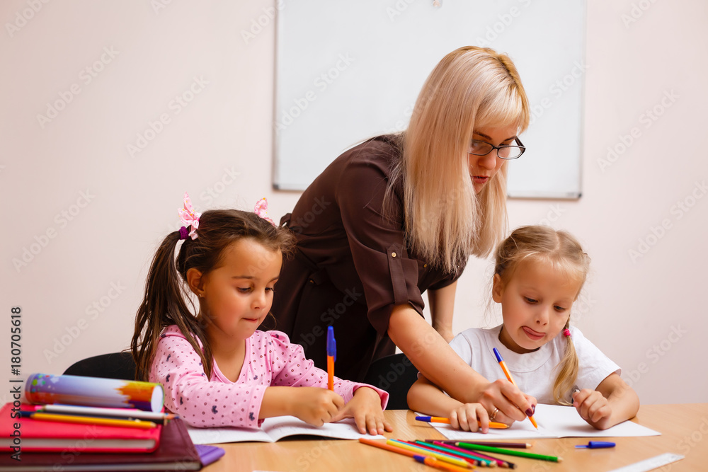 two happy little schoolgirls study in class, the teacher explains two happy little schoolgirls study in class, the teacher explains