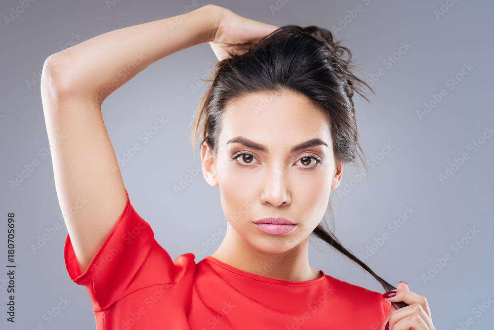 Finding image. Young beautiful pleasant woman touching her long dark hair while thinking of a new hairstyle Finding image. Young beautiful pleasant woman touching her long dark hair while thinking of a new hairstyle
