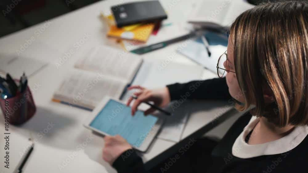 education, people children and learning concept - Close-up A schoolgirl or student uses a tablet and writes in a workbook. She's doing her homework.