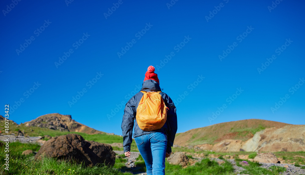 Naklejka premium back view of woman traveler on a walk in the Valley of the river of Hveragerdi Iceland. Hiking Tour of Reykjadalur Hot Springs