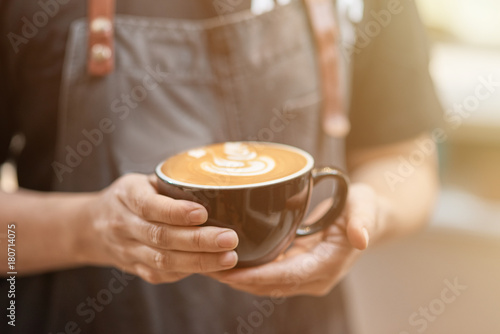 Pleasant barista holding a cup of tasty cappuccino