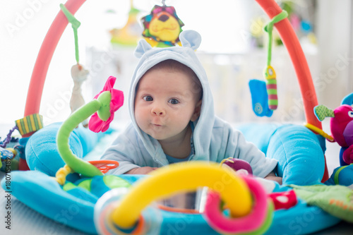 Cute baby boy on colorful gym, playing with hanging toys at home