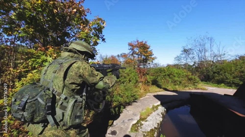 Soldier on a mission. Soldier with AK rifle seeking for enemies. Old rusty military ruins on background. photo