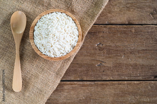 raw white sticky rice in wood bowl with wood spoon on gunny sack cloth on wooden table, top view with copy space