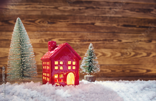 Old wooden planks with christmas trees and red house. Brown background with snow and snowflakes