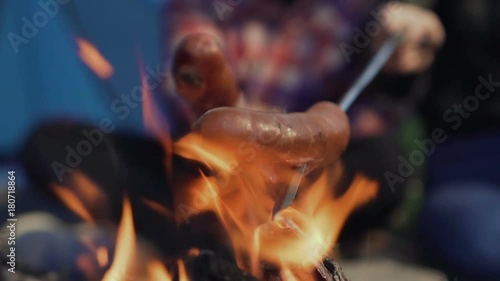 Grilling sausages over a campfire, campers roasting sausages. Tourists are sitting near the flame photo