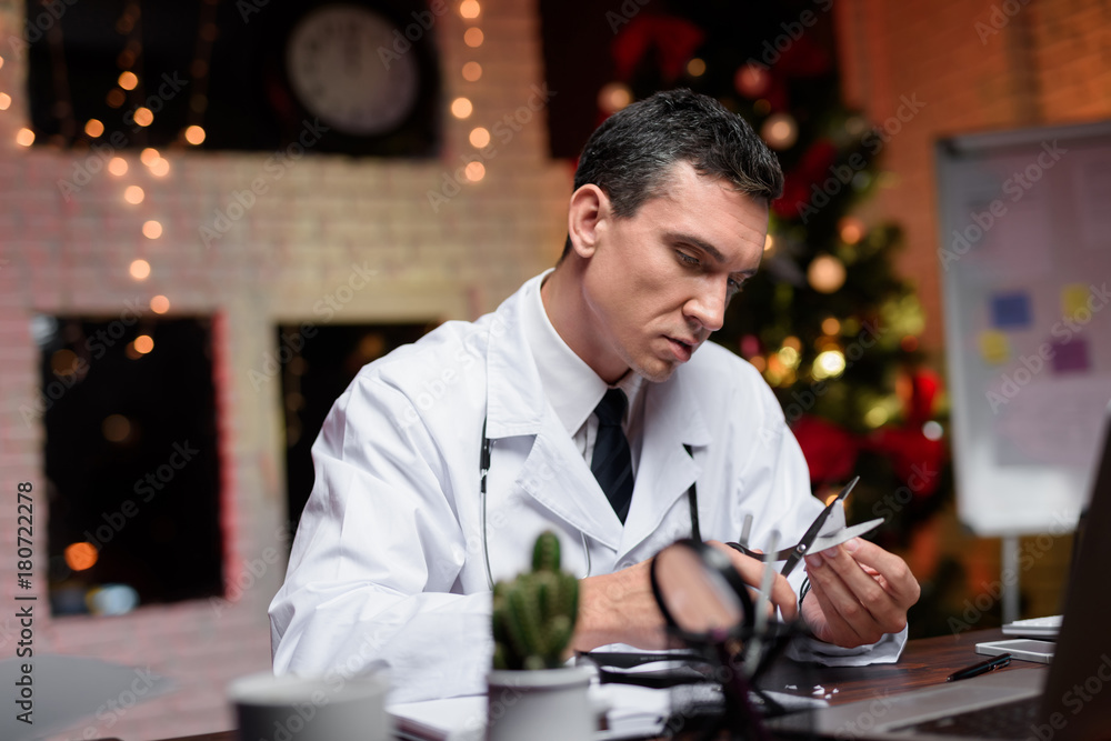 The doctor works on New Year's Eve. He holds the paper in his hands and cuts out a snowflake from it.