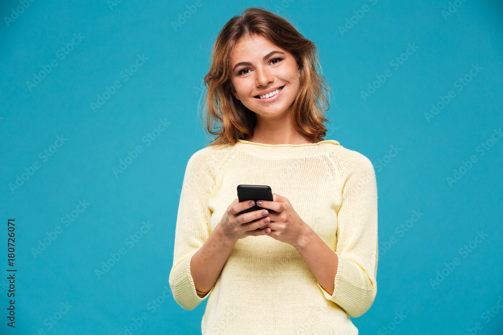 Smiling woman in sweater holding smartphone and looking at camera Smiling woman in sweater holding smartphone and looking at camera