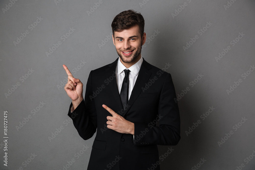 Young smiling man bearded businessman pointing with two finger upward, looking at camera Young smiling man bearded businessman pointing with two finger upward, looking at camera