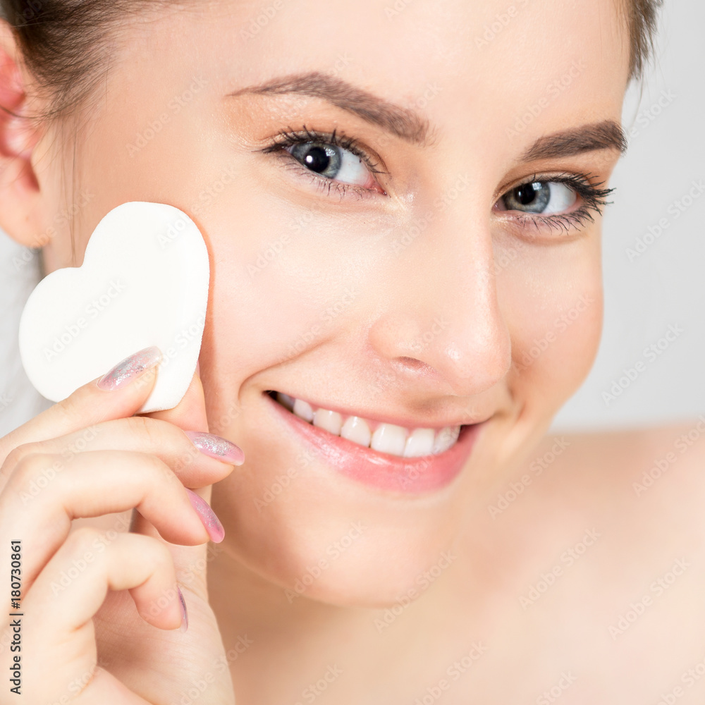 Portrait of a beautiful cheerful young woman with a sponge in the form of a heart in her hands. Her skin is fresh and healthy, and make-up is very light and natural. Photo closeup Portrait of a beautiful cheerful young woman with a sponge in the form of a heart in her hands. Her skin is fresh and healthy, and make-up is very light and natural. Photo closeup