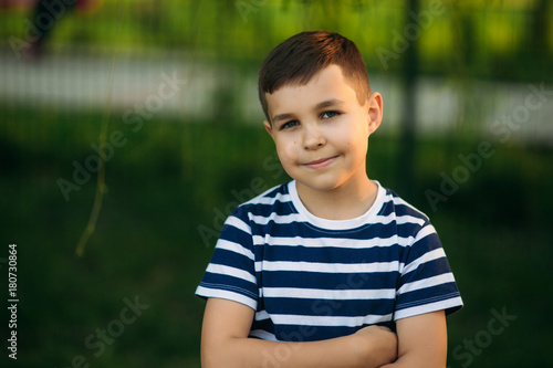 A little boy in a striped T-shirt is playing on the playground, Swing on a swing. Child is smiling and cheering