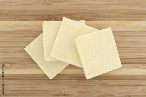 Top view of several slices of sharp cheddar cheese squares on a small wood cutting board.