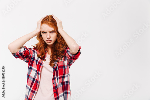 Confused ginger woman in shirt holding head and looking away