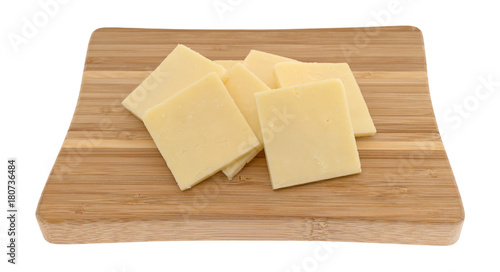 Several slices of sharp cheddar cheese squares on a small wood cutting board isolated on a white background.