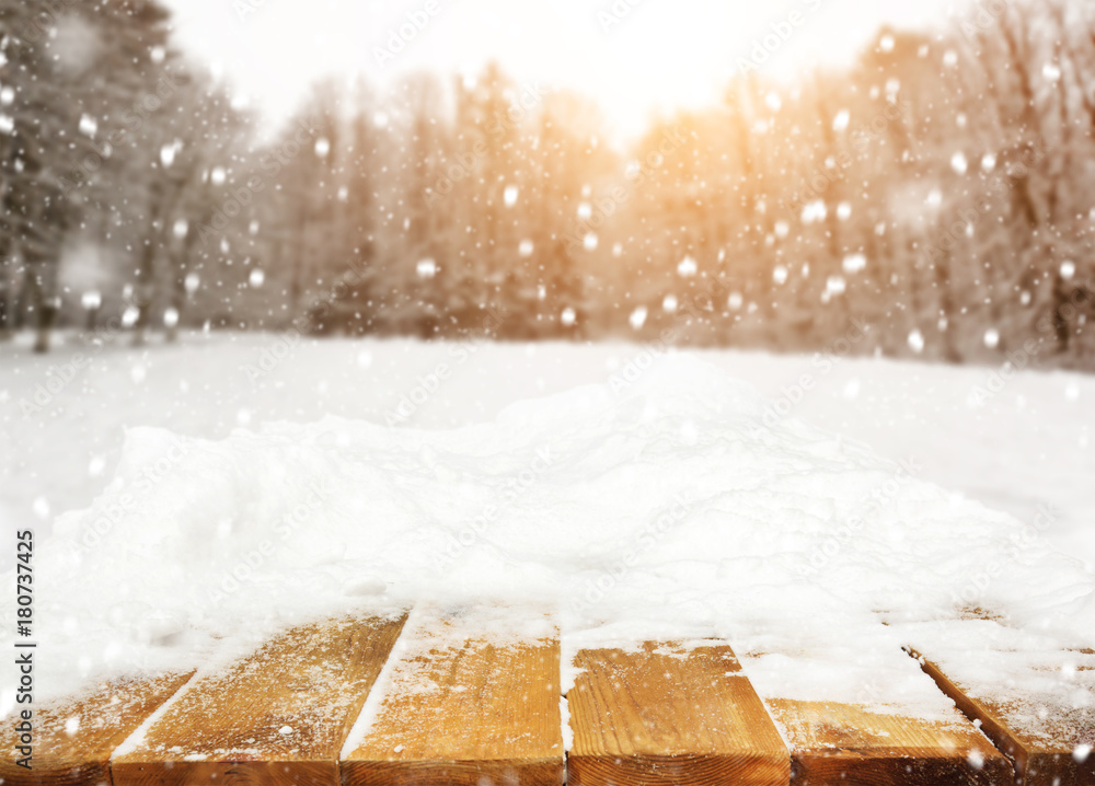 Fototapeta premium Wooden desk covered by snow and snowy park on background