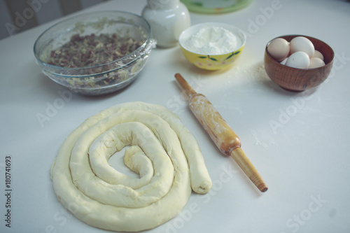 on a white table a bowl with eggs and flour, ready to be rolled up and next to the rolling pin. view from above