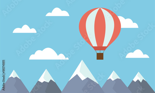 A view of a large and hot air balloon flying between clouds in a blue sky above mountain peaks