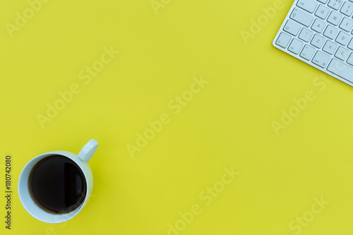 Computer keyboard and coffee cup with copy space on yellow background