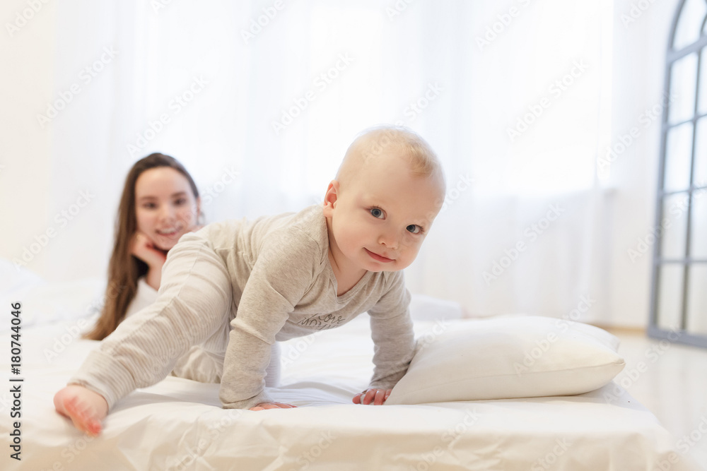 young caucasian mother Watching Baby boy in white pajama tries Take First Steps At Home. child in the foreground .Lifestyle family portrait young caucasian mother Watching Baby boy in white pajama tries Take First Steps At Home. child in the foreground .Lifestyle family portrait