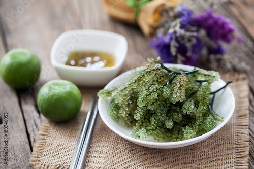 sea grapes or green caviar with spicy sauce on wooden background