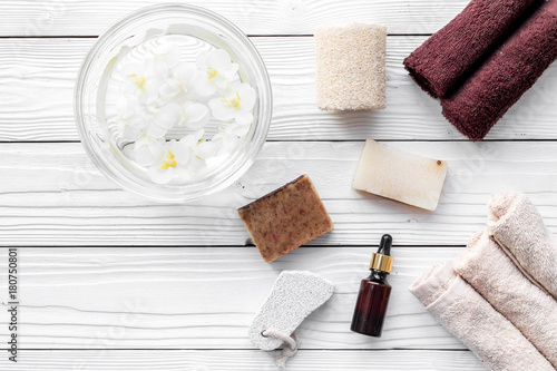 Bath in bowl with tropical flowers for foot spa, pumice stone, soap and oil on white wooden background top view copyspace