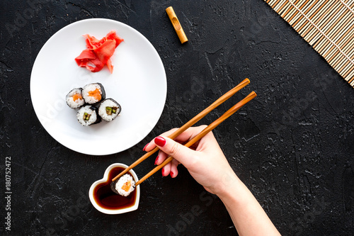 Hand takes sushi roll with salmon and avocado with chopstick. Black background top view