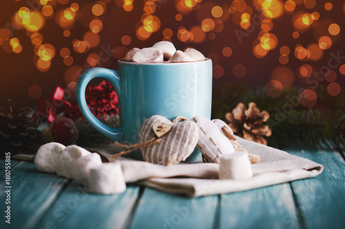 Blue mug filled with hot chocolate with marshmallow candies. Lights on background