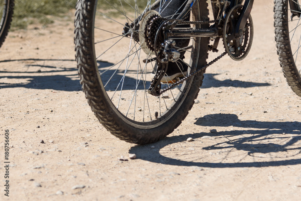 Bicycle wheel close-up and foot on pedal of bicycle against the background of a dirt road Bicycle wheel close-up and foot on pedal of bicycle against the background of a dirt road