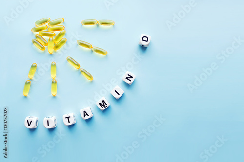 Yellow capsules in the form of the sun with rays and the word vitamin D from white cubes with letters on a blue background. VITAMIN D word for healthy and medical concept. Sunshine vitamin
