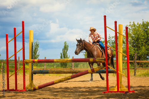 Cowgirl in western hat doing horse jumping