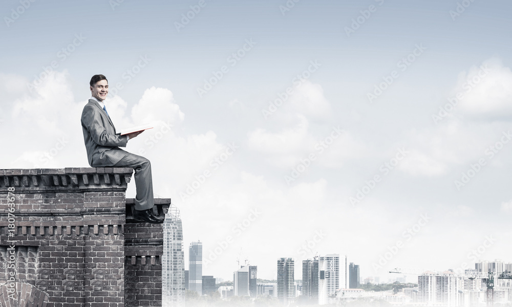 Man on roof edge reading book and cityscape at background Man on roof edge reading book and cityscape at background