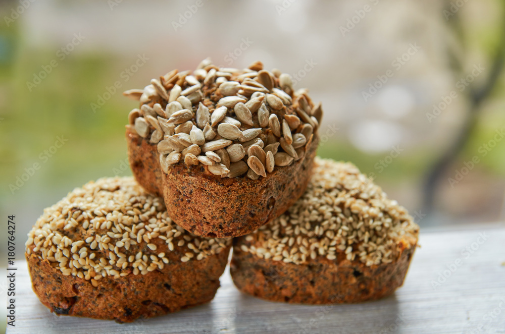 Three freshly baked raisins cakes with sesame and sunflower seeds isolated on gray wooden table. Three muffins on blurred nature background. Close up view Three freshly baked raisins cakes with sesame and sunflower seeds isolated on gray wooden table. Three muffins on blurred nature background. Close up view