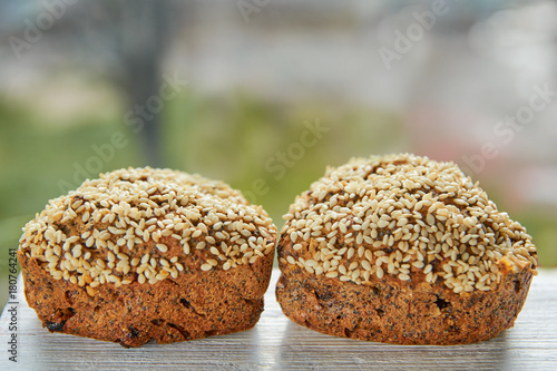 Two freshly baked raisins cakes with sesame seeds isolated on gray wooden table. Two mafines on blurred nature background. Close up view