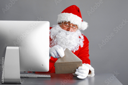 Santa Claus reading children letters and writing responses to them using laptop
