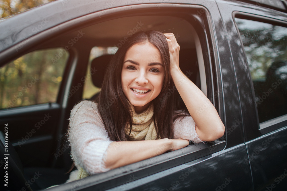 Long-haired brunette on the auto background. A female model is wearing a sweater and a scarf. Autumn concept. Autumn forest journey by car Long-haired brunette on the auto background. A female model is wearing a sweater and a scarf. Autumn concept. Autumn forest journey by car