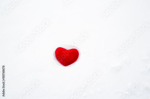 Red plush heart abandoned on white snow.