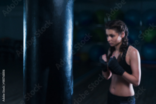 Young fighter boxer fit girl wearing hand bandage in training with heavy punching bag in gym in bokeh. Focus on punching bad © Igor Kardasov