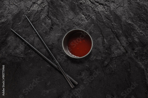 Wooden chopsticks and sweet and sour sauce bowl on black slate stone.
