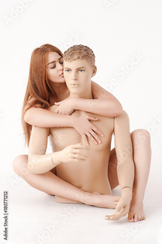 Red-haired, naked, young, a woman hugs the mannequin of a man with her hands and feet and whispers into his ear. On a white background. The concept of relations photo