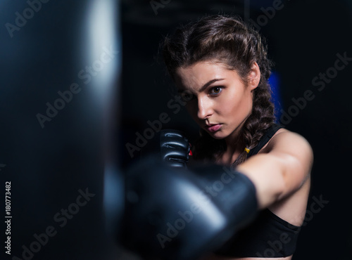 Beautiful fighter boxer fit girl wearing boxing gloves in training with heavy punching bag in gym. Low key image. Woman power © Igor Kardasov