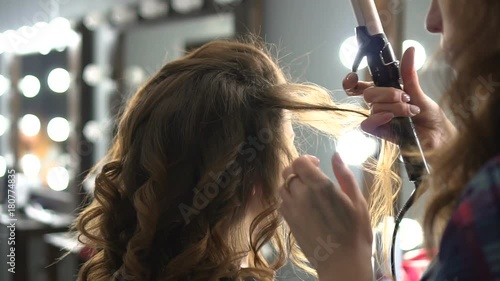 Hairdresser doing wrap curling brown hair in a beauty salon with iron photo