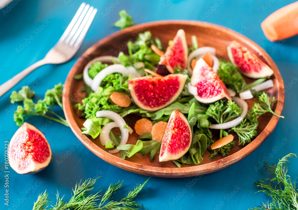 Autumn salad of arugula, figs in a brown earthenware plate on a blue background. top view Autumn salad of arugula, figs in a brown earthenware plate on a blue background. top view