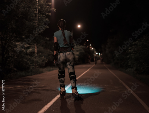 Sports roller girl skating at night using flashlight or torchlight. She is searching for way on the road.