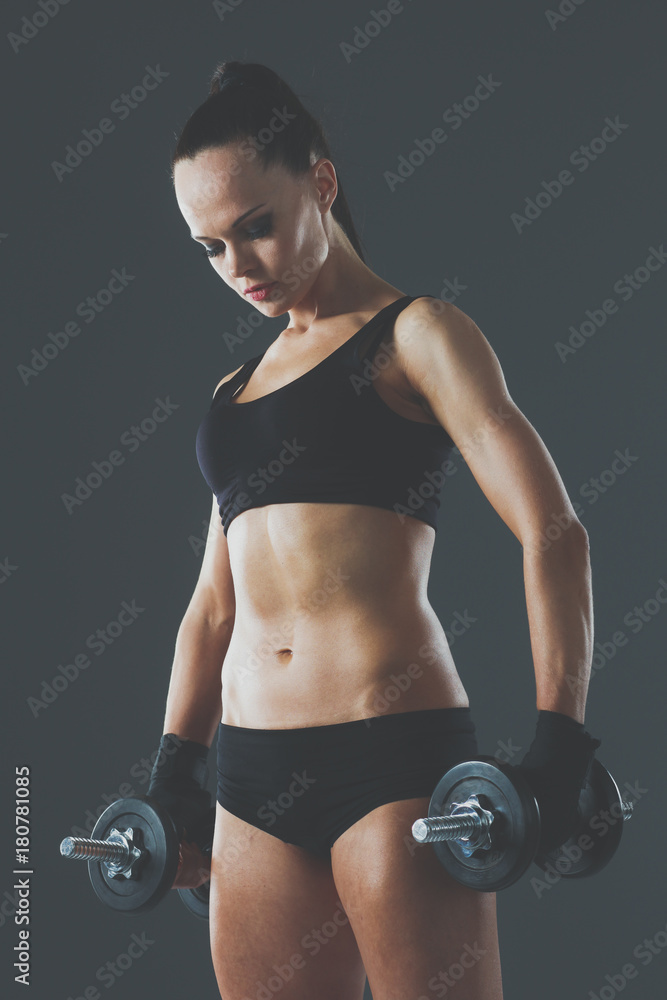 Muscular young woman standing on gray background. Muscular young woman Muscular young woman standing on gray background. Muscular young woman